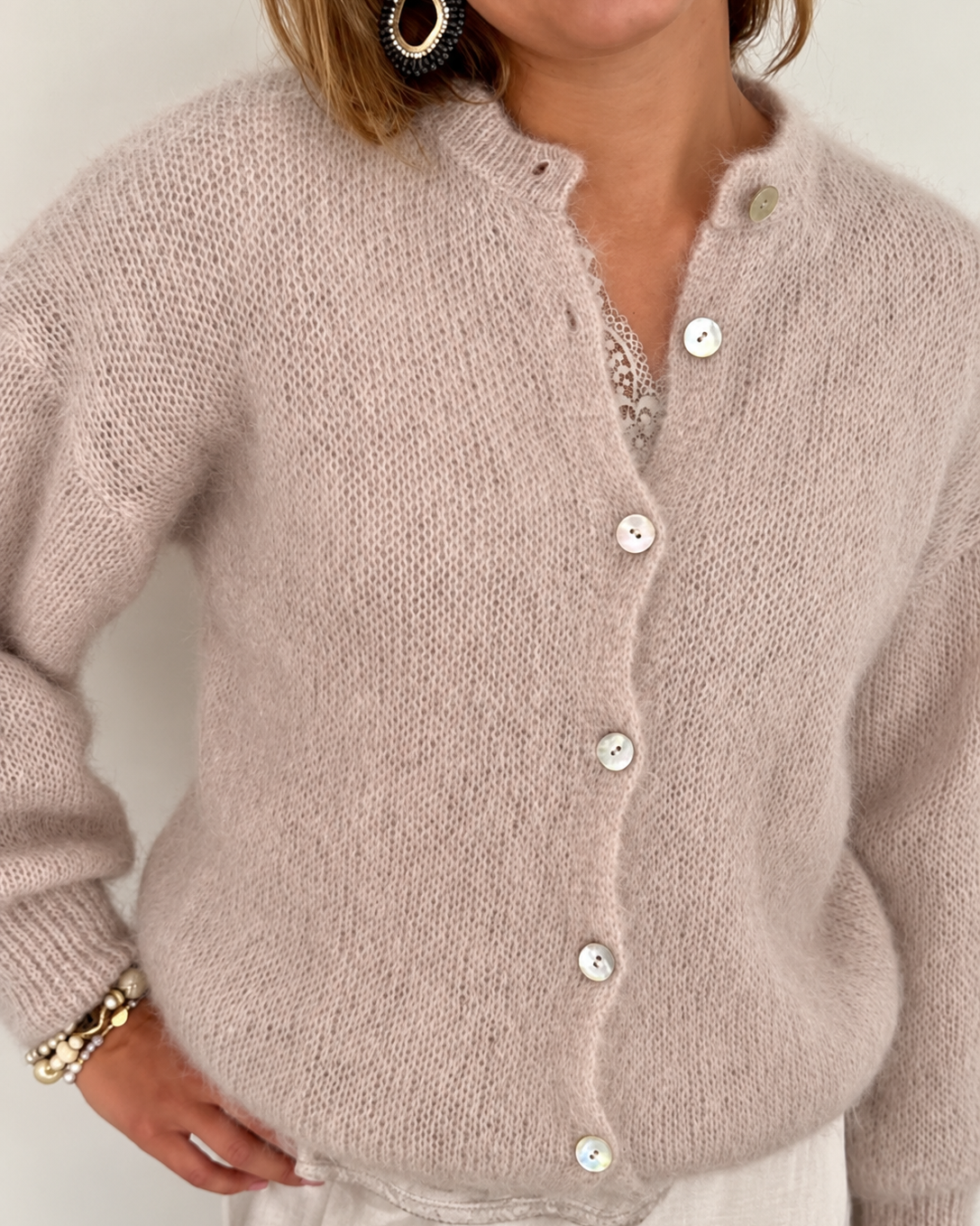 Peura Collection Nelly beige mohairneuletakki naisen päällä. Pehmeä, pörröinen neule, jossa on V-pääntie, helmiäisnapit ja pitkät hihat.